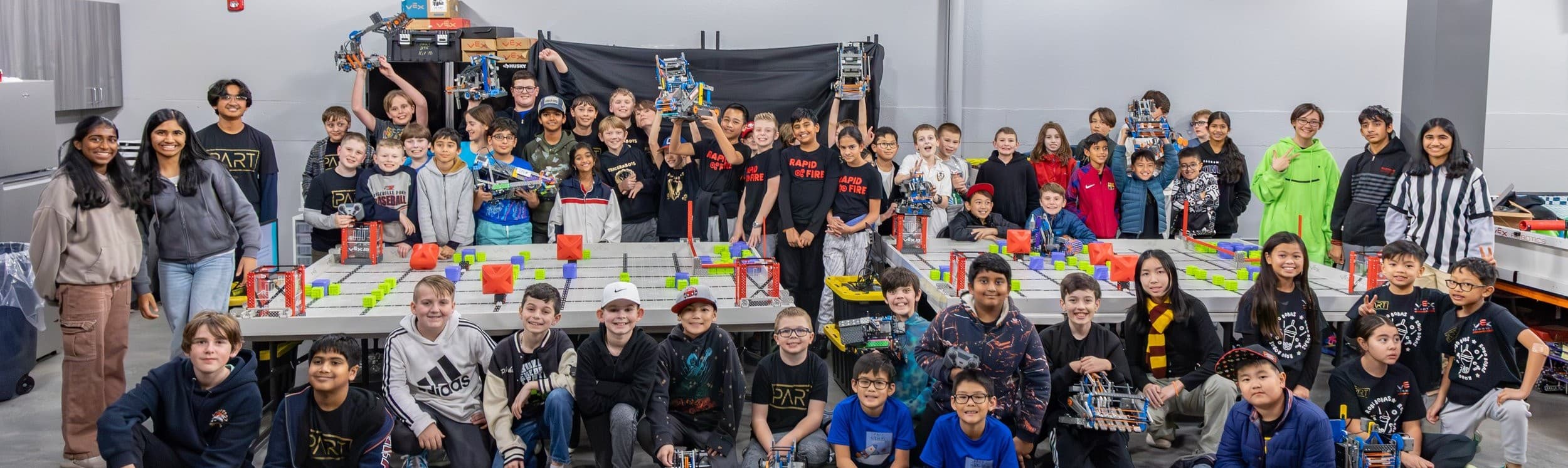 Dozens of Placer Robotics VEX IQ students with their robots around competition fields at a league night