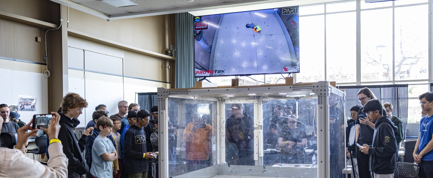 The full antweight and beetleweight combat arena at Sacramento Bot Battles, with the overhead match feed on screen and spectators around the cage