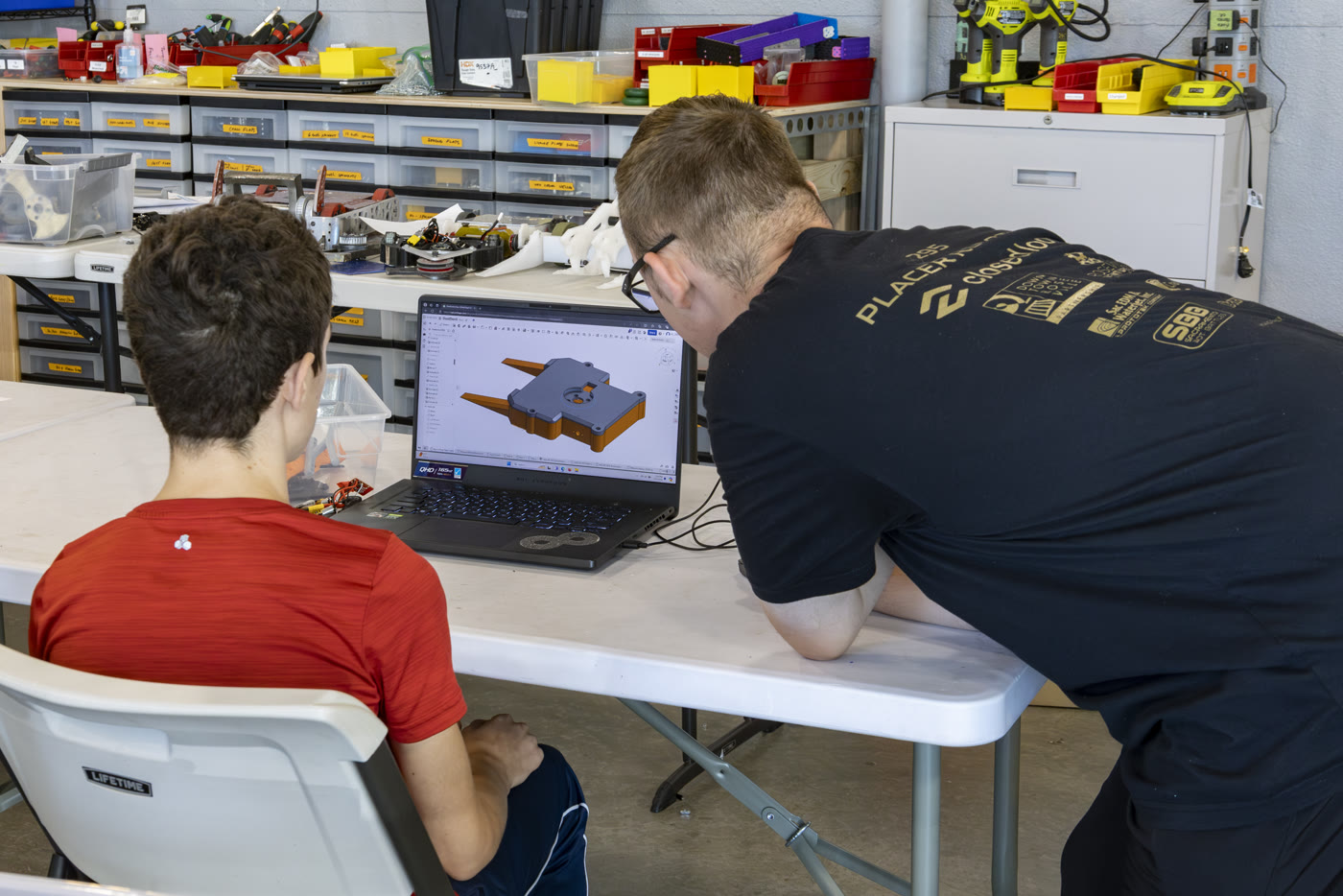 Two students at a laptop in the Placer Robotics lab, reviewing a combat robot baseplate in CAD